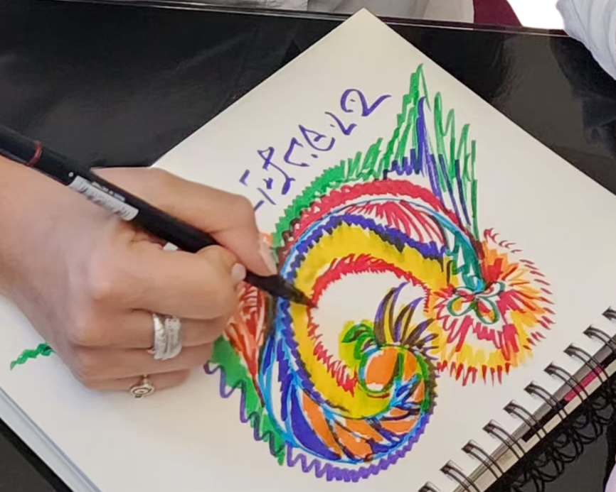 A person drawing a colorful dragon in a sketchbook.