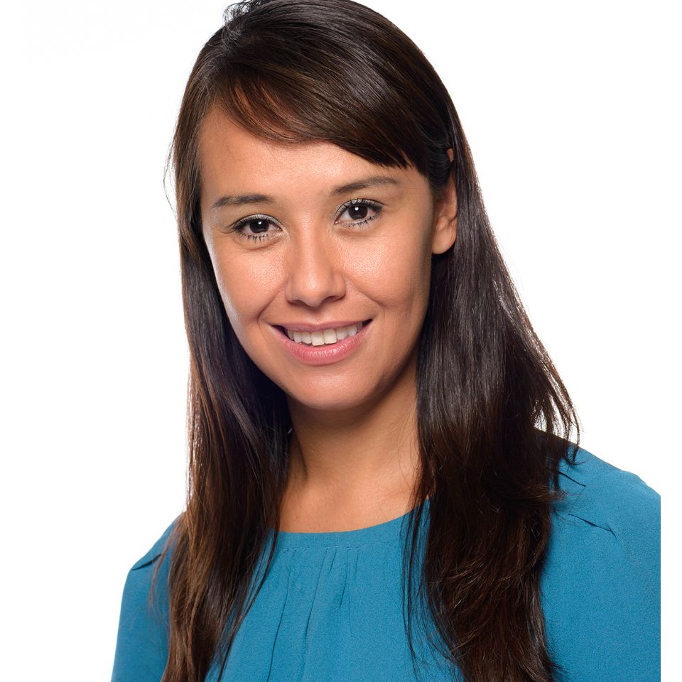 A smiling woman with long dark hair wearing a teal blouse.